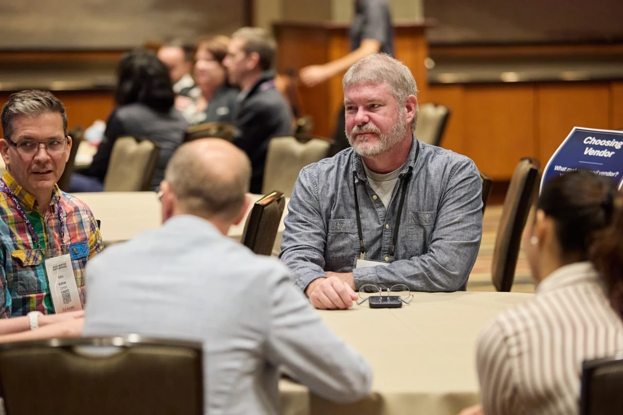 Attendees discuss vendor selection around a table beside a Choosing a Vendor sign