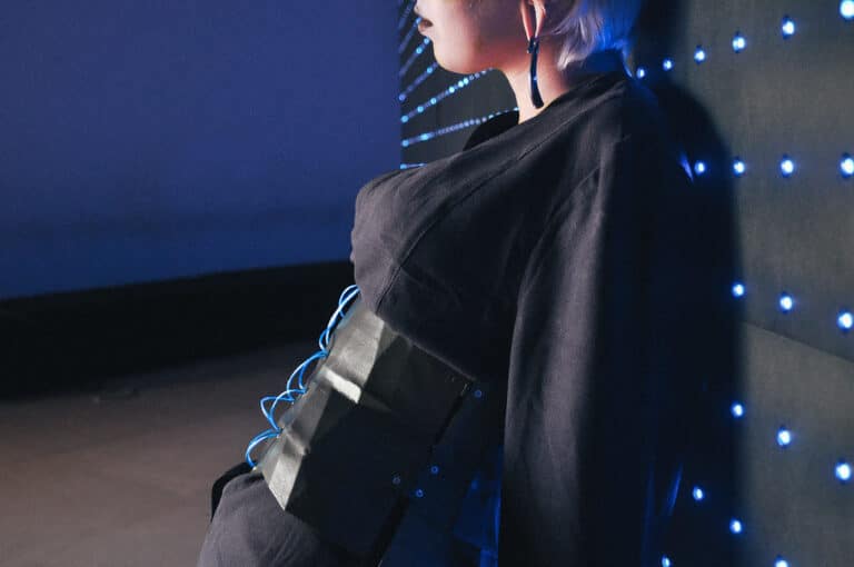 A person wearing a hooded jacket stands in front of a night sky with twinkling lights, creating a dramatic and moody atmosphere.