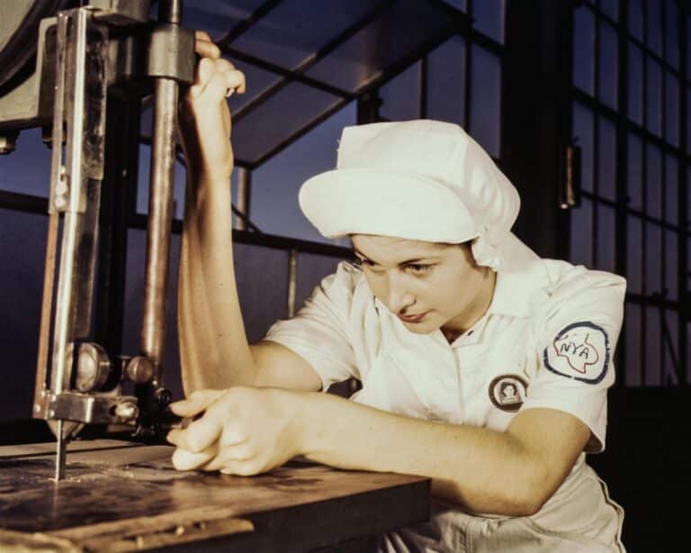 A woman in a white uniform and cap operating a vintage machine in an industrial setting
