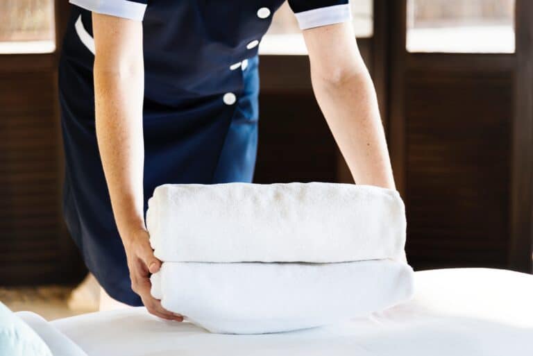Hotel employee holding a stack of clean white towels in a hotel room