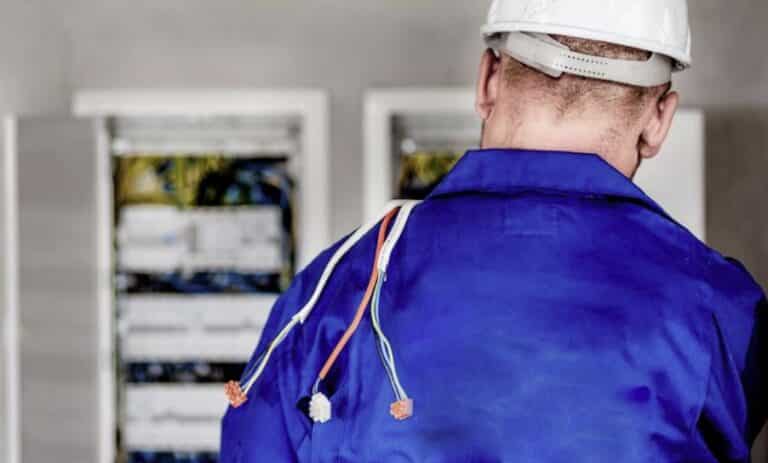A construction worker wearing a blue uniform and hard hat, facing away from the camera, standing in front of construction equipment.