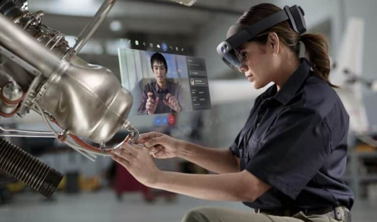A woman wearing virtual reality goggles and a black uniform interacting with a futuristic computer interface in an industrial setting
