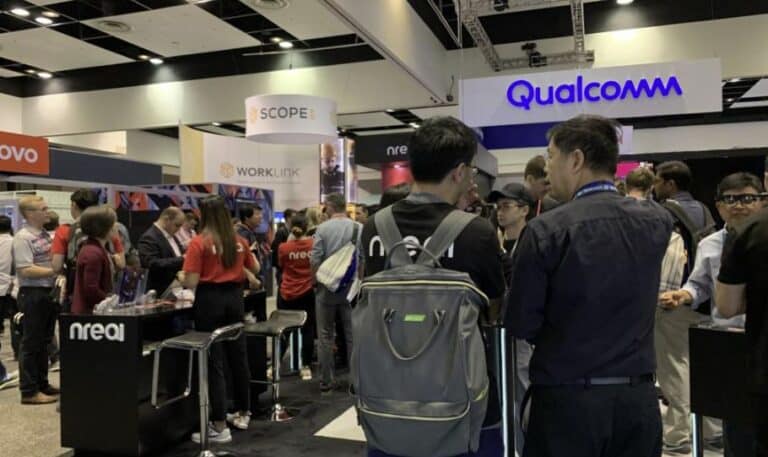 Busy technology trade show booth with Qualcomm and nreal branding, people gathered around and inspecting products