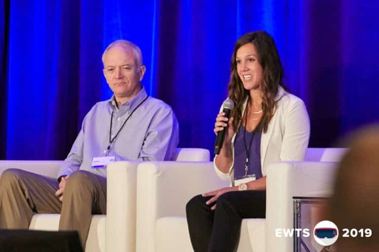 Two people on stage at a conference, a man in a collared shirt and a woman with a microphone speaking.