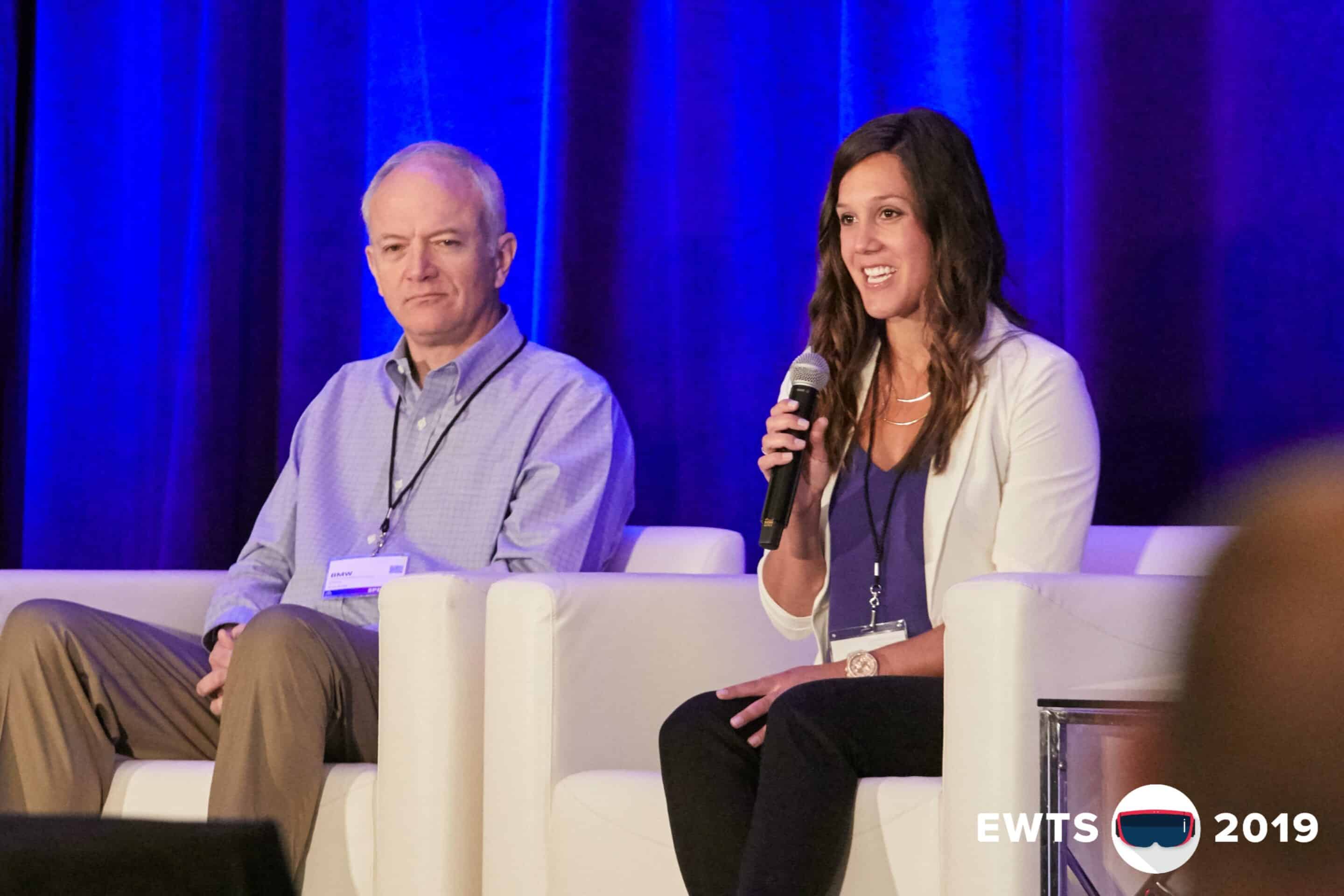 Two people on stage at a conference, a man in a collared shirt and a woman with a microphone speaking.