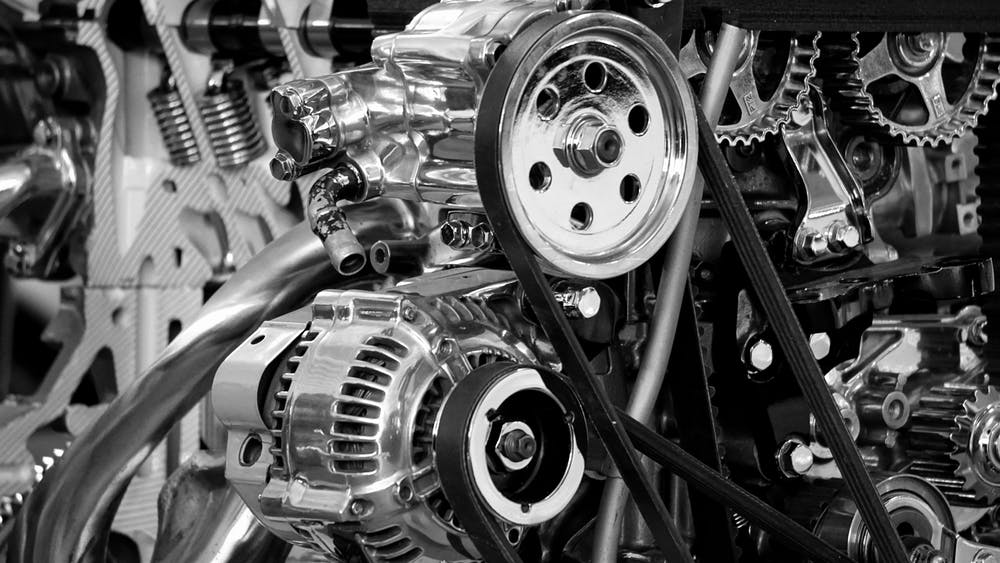 Close-up view of a car engine with various mechanical parts and components, such as gears, belts, and cylinders, in black and white.