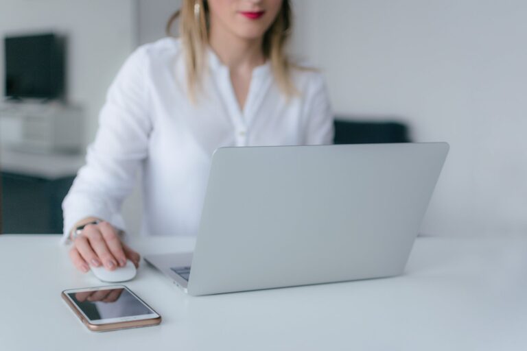 Woman working on laptop computer at desk with smartphone