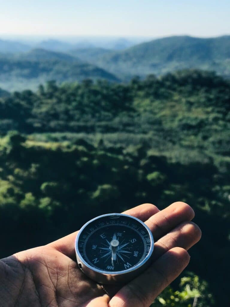 Hand holding a compass overlooking a scenic mountain landscape
