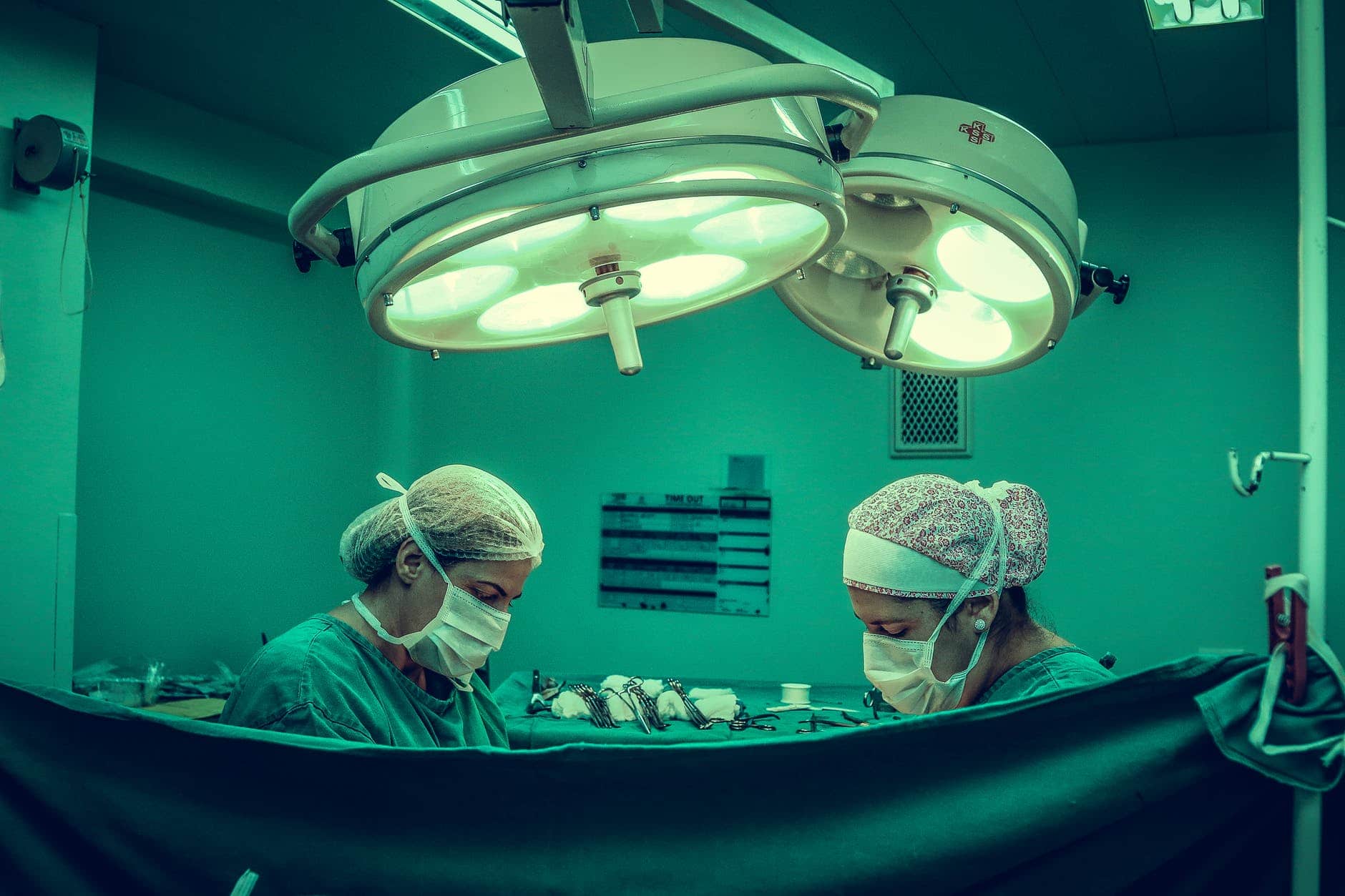 Two medical professionals perform surgery under bright overhead operating room lights