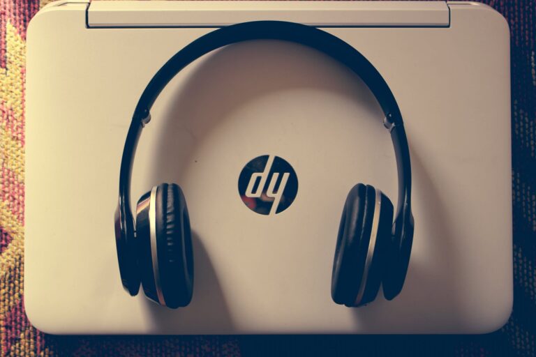 A pair of black headphones with the HP logo visible on the headband, sitting on a white laptop or notebook computer