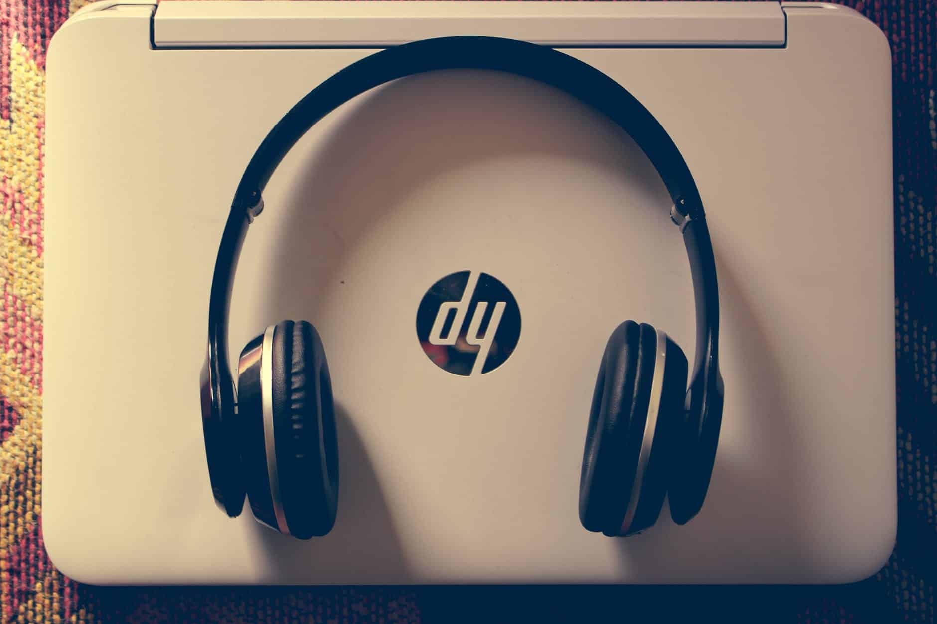 A pair of black headphones with the HP logo visible on the headband, sitting on a white laptop or notebook computer