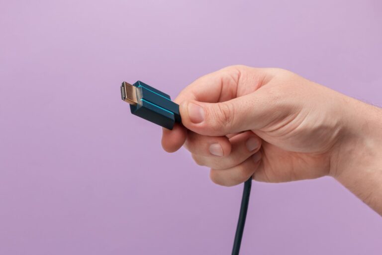 Hand holding a HDMI cable connector on a purple background