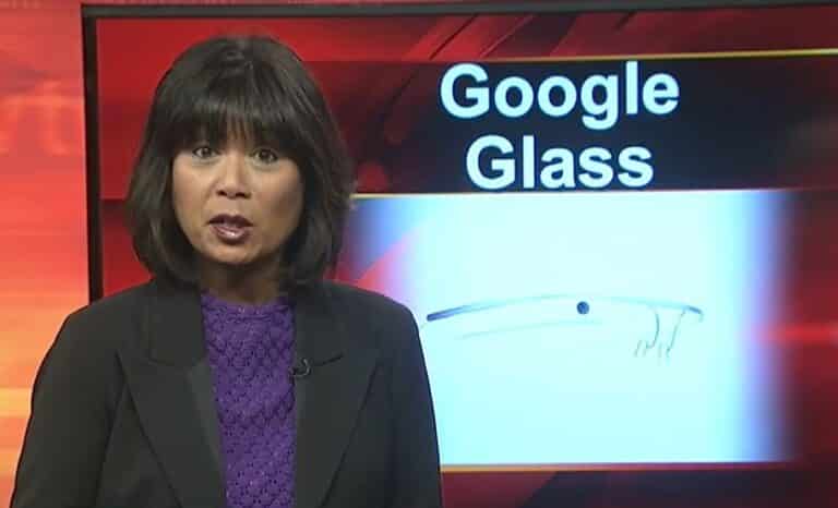 A woman in a purple sweater standing in front of a television studio backdrop with the Google Glass logo.