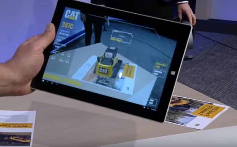 A digital tablet displays a 3D model of a Caterpillar 289C compact track loader, showcasing the machine's features and capabilities.