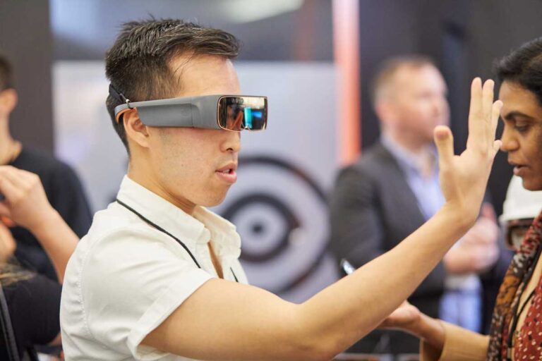 A man wearing virtual reality goggles, interacting with a virtual display in a technology expo