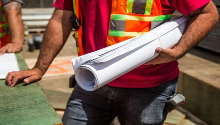 Construction worker holding blueprints, wearing high visibility safety vest