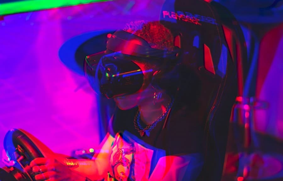A person wearing a virtual reality headset and gloves, surrounded by colorful lighting in a darkened room