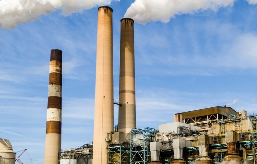 Tall industrial smokestacks and chimneys against a blue sky with clouds