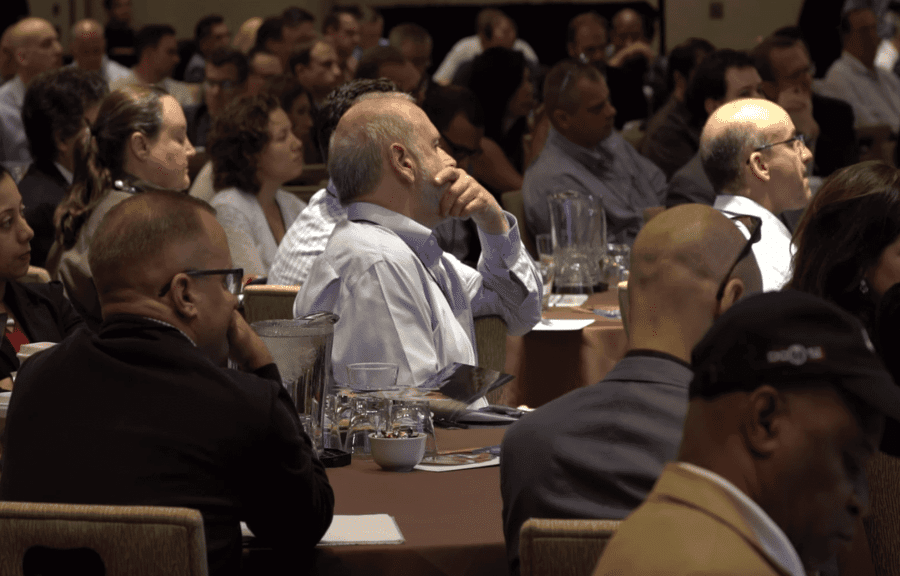 A large crowd of people seated at tables in a formal setting, possibly a conference or event.