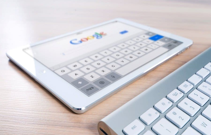 A Google tablet with a keyboard on a wooden desk, showcasing the Google search engine interface