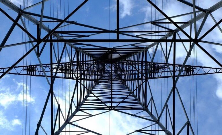 Striking silhouette of a power transmission tower against a bright blue sky with fluffy white clouds