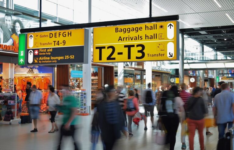 Busy airport terminal with travelers, gate signs, baggage hall, and transfer directions