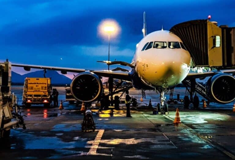A large commercial aircraft parked at the airport at night, with ground crew and equipment visible around it.