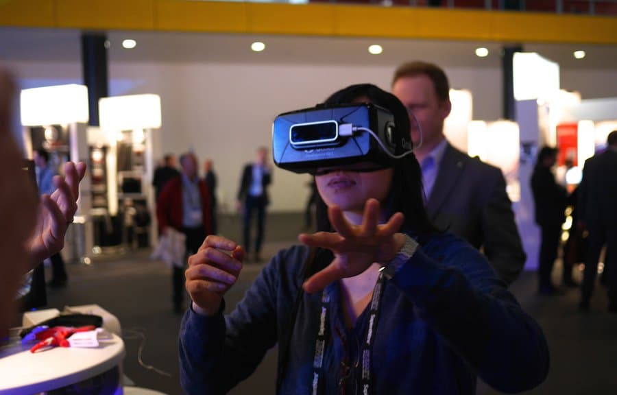 A man wearing a virtual reality headset, gesturing with his hands while experiencing a virtual reality demonstration at a technology expo