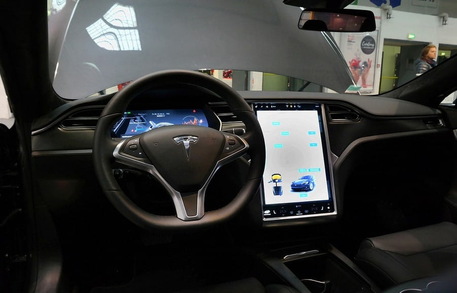 Interior of a Tesla electric vehicle with a large touchscreen display and steering wheel showing advanced technology features