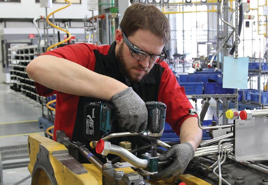 A man in a red shirt and safety glasses working on an industrial machine in a factory setting