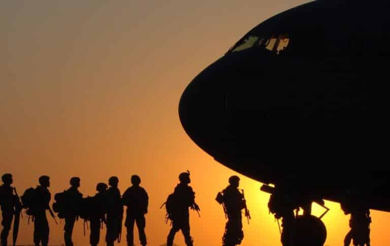 Silhouetted soldiers standing near a large aircraft at sunset