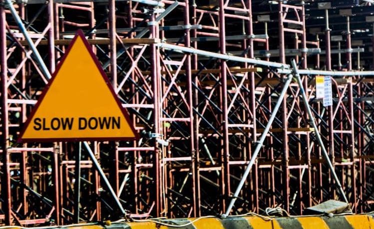 A yellow triangular 'Slow Down' warning sign mounted on a complex network of metal scaffolding and beams
