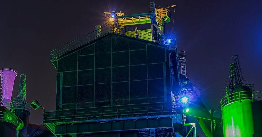 Illuminated industrial machinery and structures at night, with bright lights and colorful accents