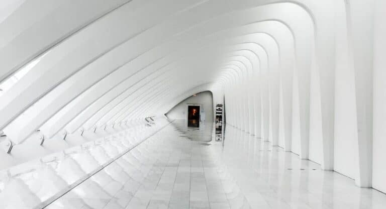 A long, white, futuristic-looking corridor with a glowing red light at the end
