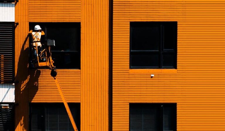 An orange industrial building with a worker on a lift, keywords: industrial, construction, building