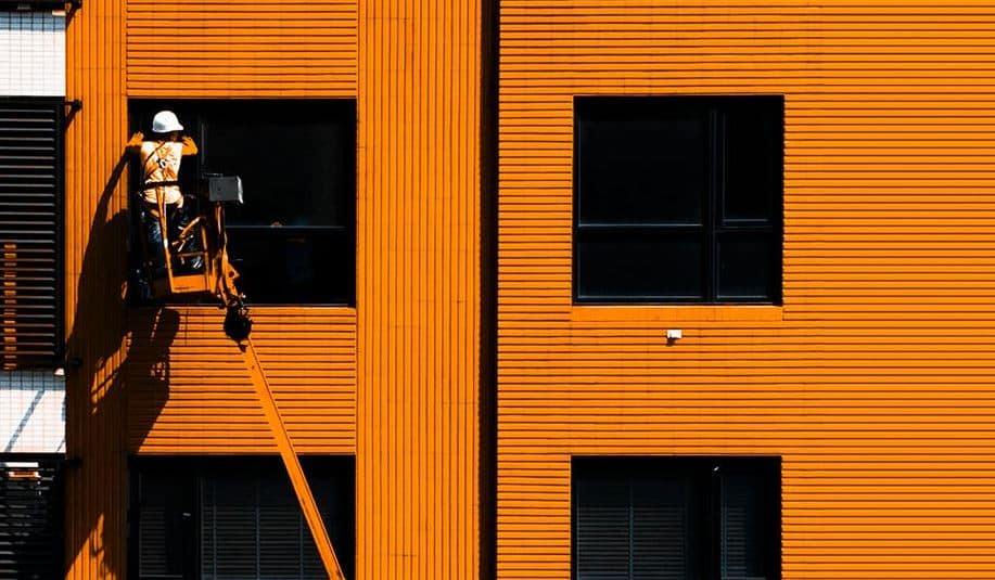 An orange industrial building with a worker on a lift, keywords: industrial, construction, building