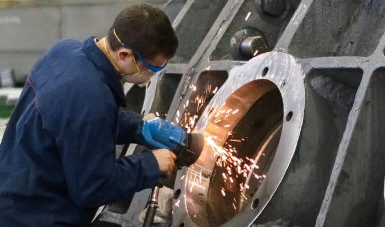 A welder in protective gear grinding metal in a workshop