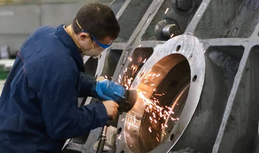 A welder in protective gear grinding metal in a workshop