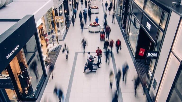 Bustling indoor shopping mall with people walking, stores, and blurred motion