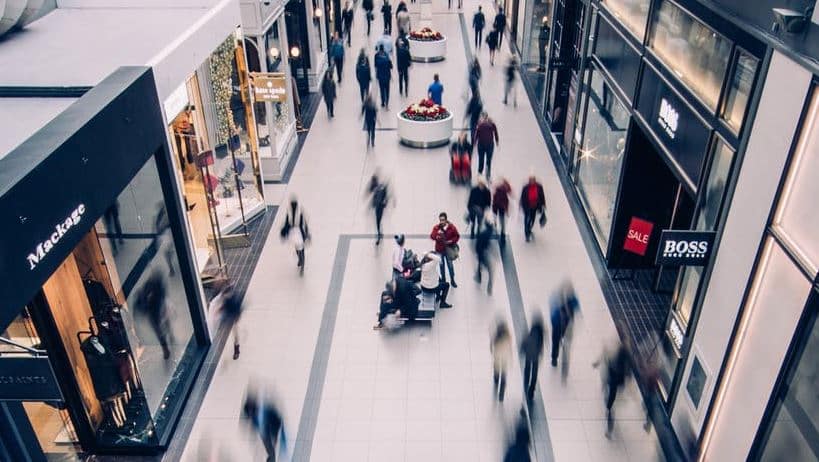 Bustling indoor shopping mall with people walking, stores, and blurred motion