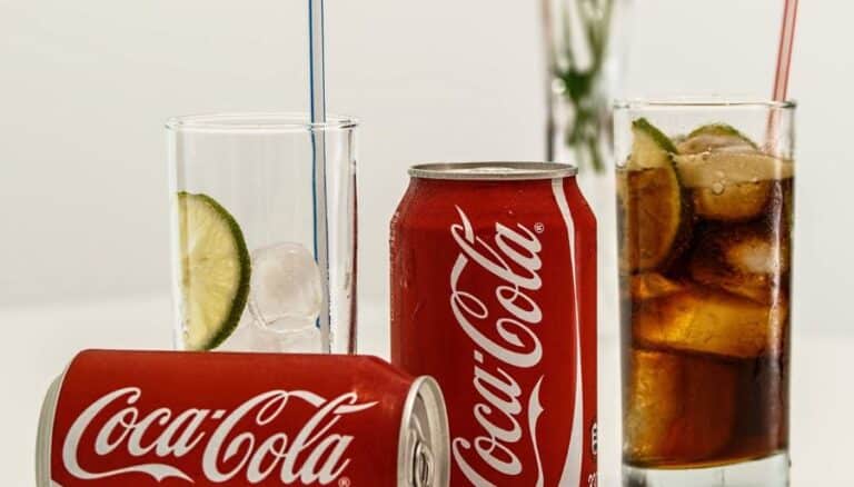 Two cans of Coca-Cola and glasses of Coke with ice and lemon slices