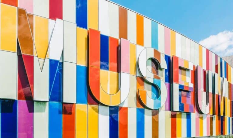 Colorful abstract mural with large letters spelling out 'MUSEO' on a facade of a building against a blue sky with clouds