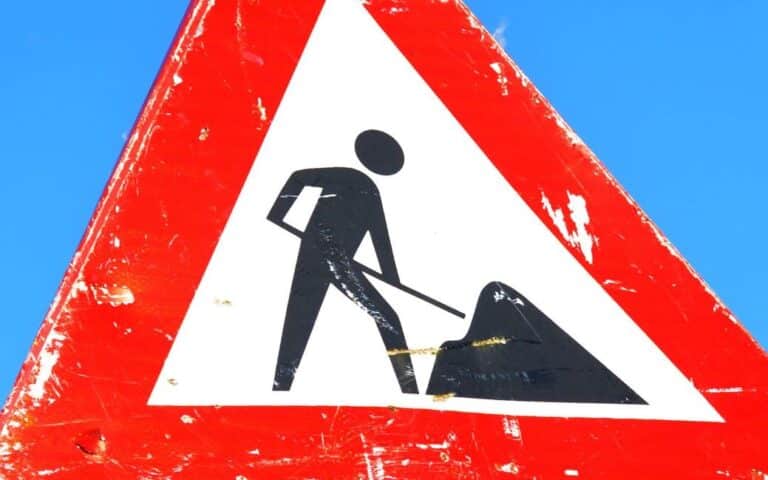 Red and white road sign showing a person with a shovel, indicating road construction or maintenance work ahead