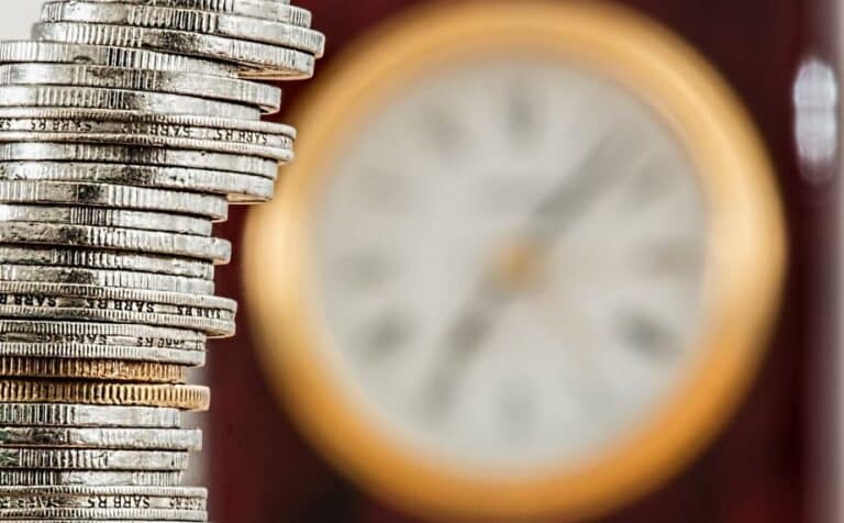 A stack of silver coins with a blurred, round clock in the background