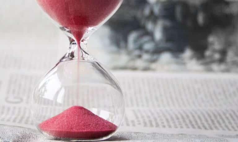 An hourglass with red sand flowing through the glass, set on a blurred newspaper background