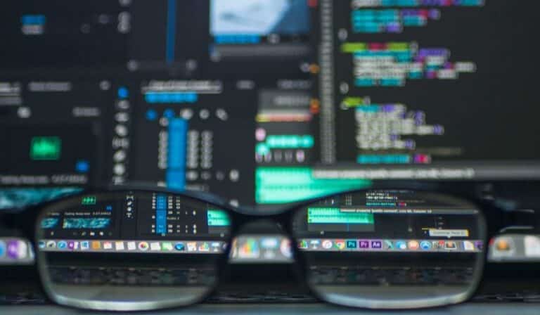 Closeup view of a computer screen and keyboard, showing various software interfaces and programming code, as seen through a pair of glasses