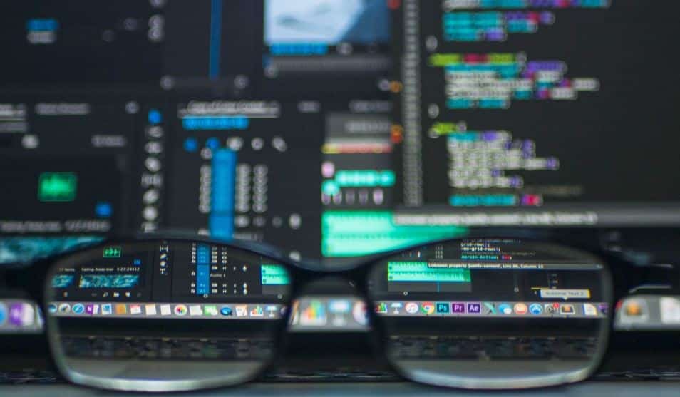 Closeup view of a computer screen and keyboard, showing various software interfaces and programming code, as seen through a pair of glasses