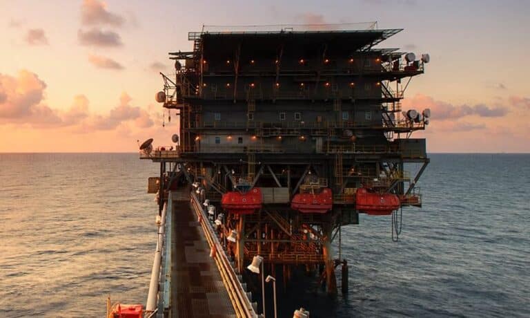 Offshore oil platform at sunset, with various equipment and structures visible against a cloudy sky over the open ocean