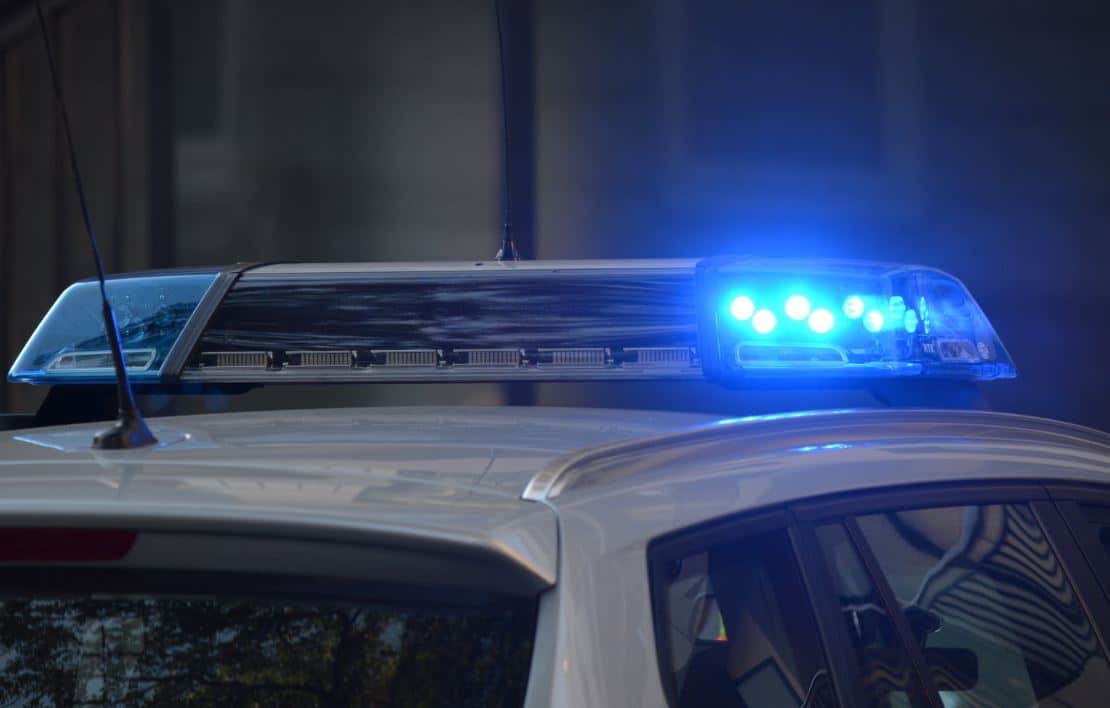 A close-up view of a police car's flashing blue and white lights mounted on its roof, signaling emergency response