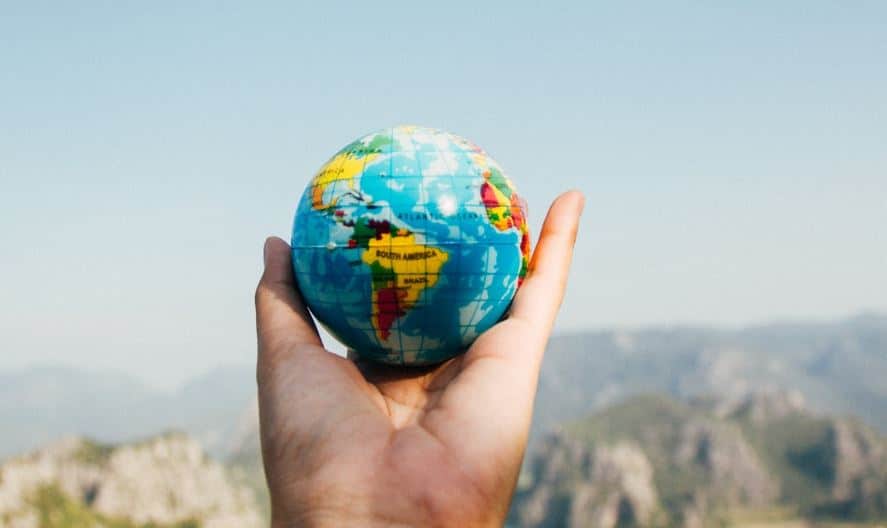 A hand holding a miniature globe showing the continents of the world